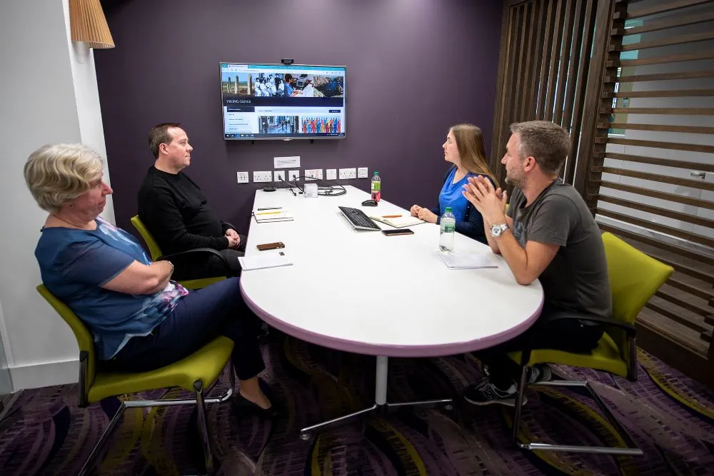 Team meet around table looking at large screen TV image of website